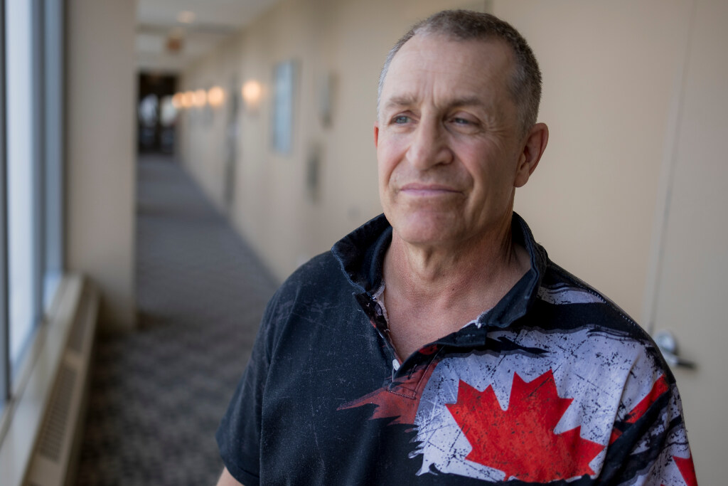 Doug Smerek stands in a beige hallway while wearing a collared shirt with the Canadian flag on it.